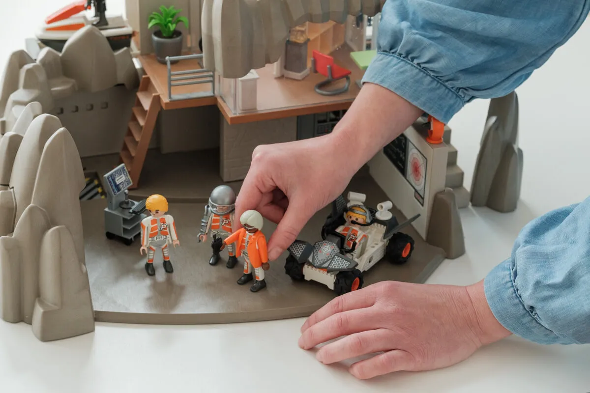 Eine Hand positioniert eine Playmobil-Figur auf einem Spiel, das auf einem weißen Tisch steht